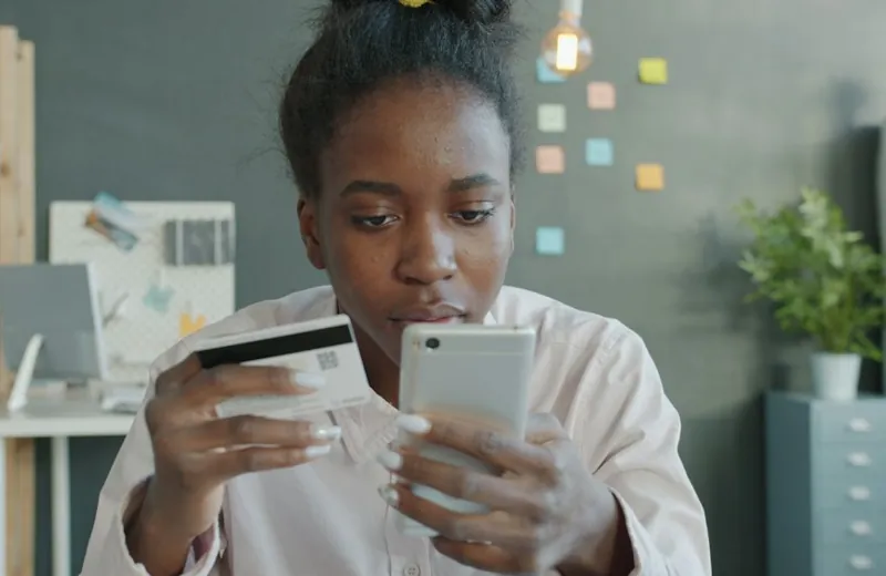 A young woman paying online with her phone and a bank card